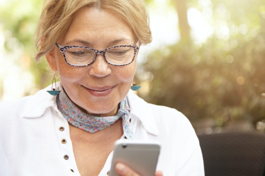 Attractive smiling elderly woman wearing spectacles typing message or checking e-mail, using wireles